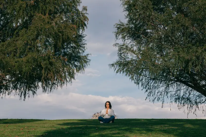 Cecilia Pederzolli meditando sentada en el pasto entre dos árboles
