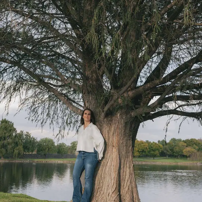 Cecilia Pederzolli recargada en un árbol grande junto a un lago
