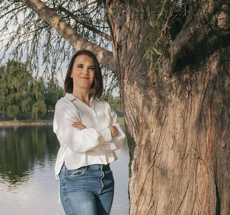 Cecilia Pederzolli con los brazos cruzados junto a un árbol y un lago