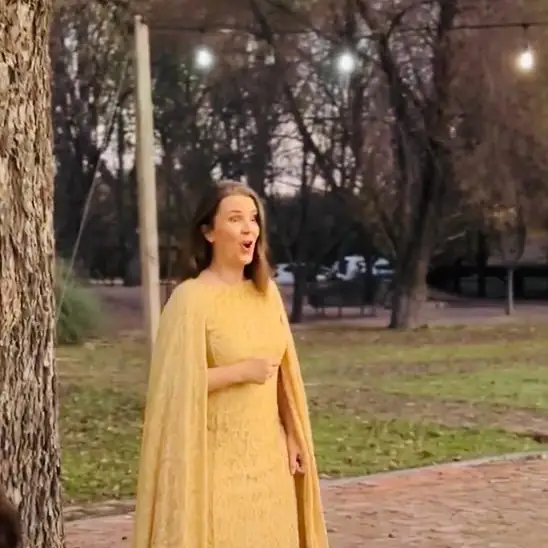 Cecilia Pederzolli con vestido amarillo y capa en un jardín al atardecer